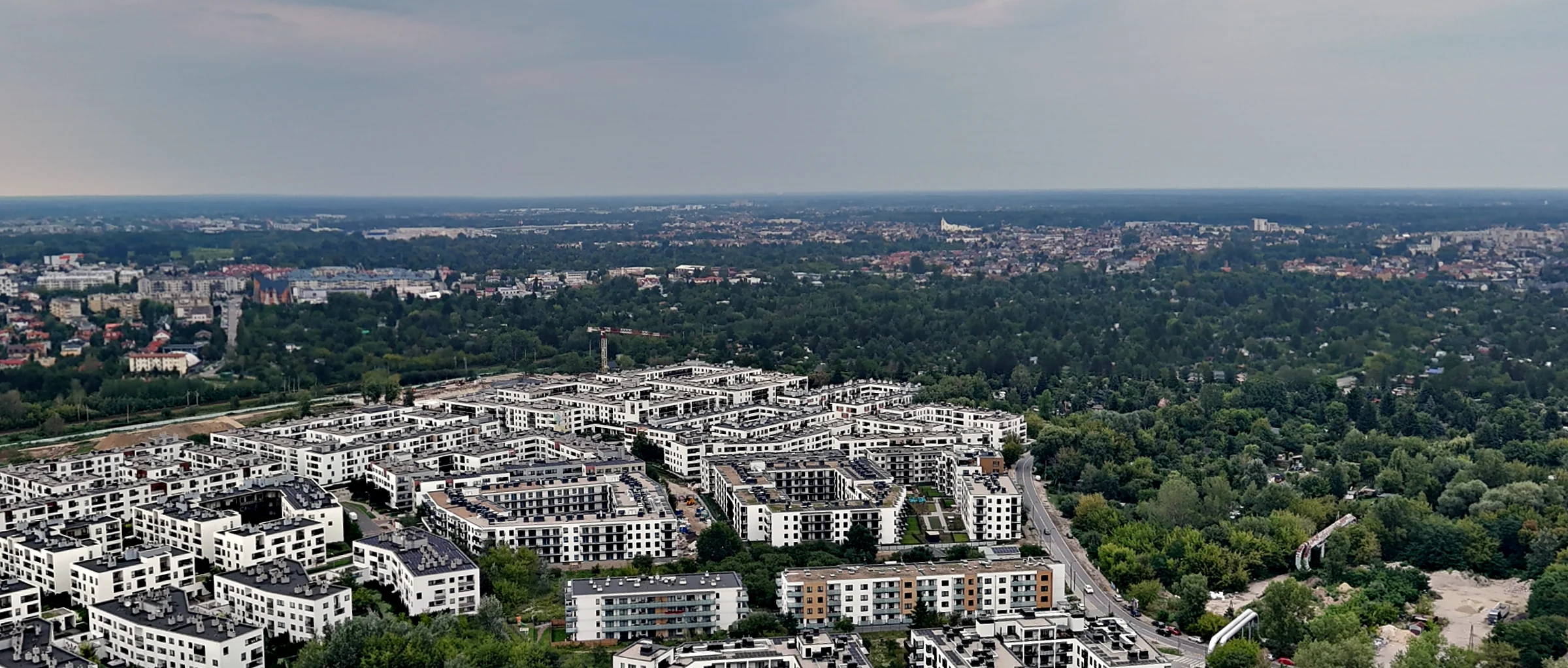 Osiedle po lewej, pas drzew po prawej, miasto po horyzont — zdjęcie z drona, 1 sierpnia 2026